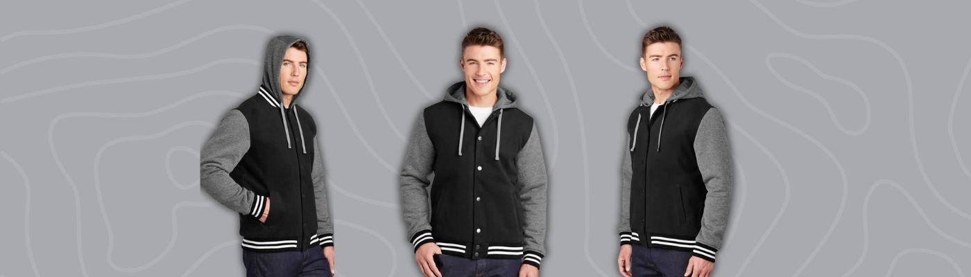 Model wearing a black and gray custom letterman jacket with striped cuffs and hem from Sport-Tek, showcasing a retro collegiate style for corporate branding..