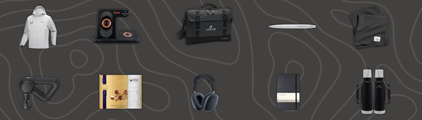Flat lay of premium new year corporate gifts including branded jacket, tech accessories, headphones, notebook, pen, and gift hampers on dark background, as part of new year corporate gifts.