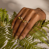 Croissant Dome Ring on Brown Skin Model Hand Touching a Koru Plant.