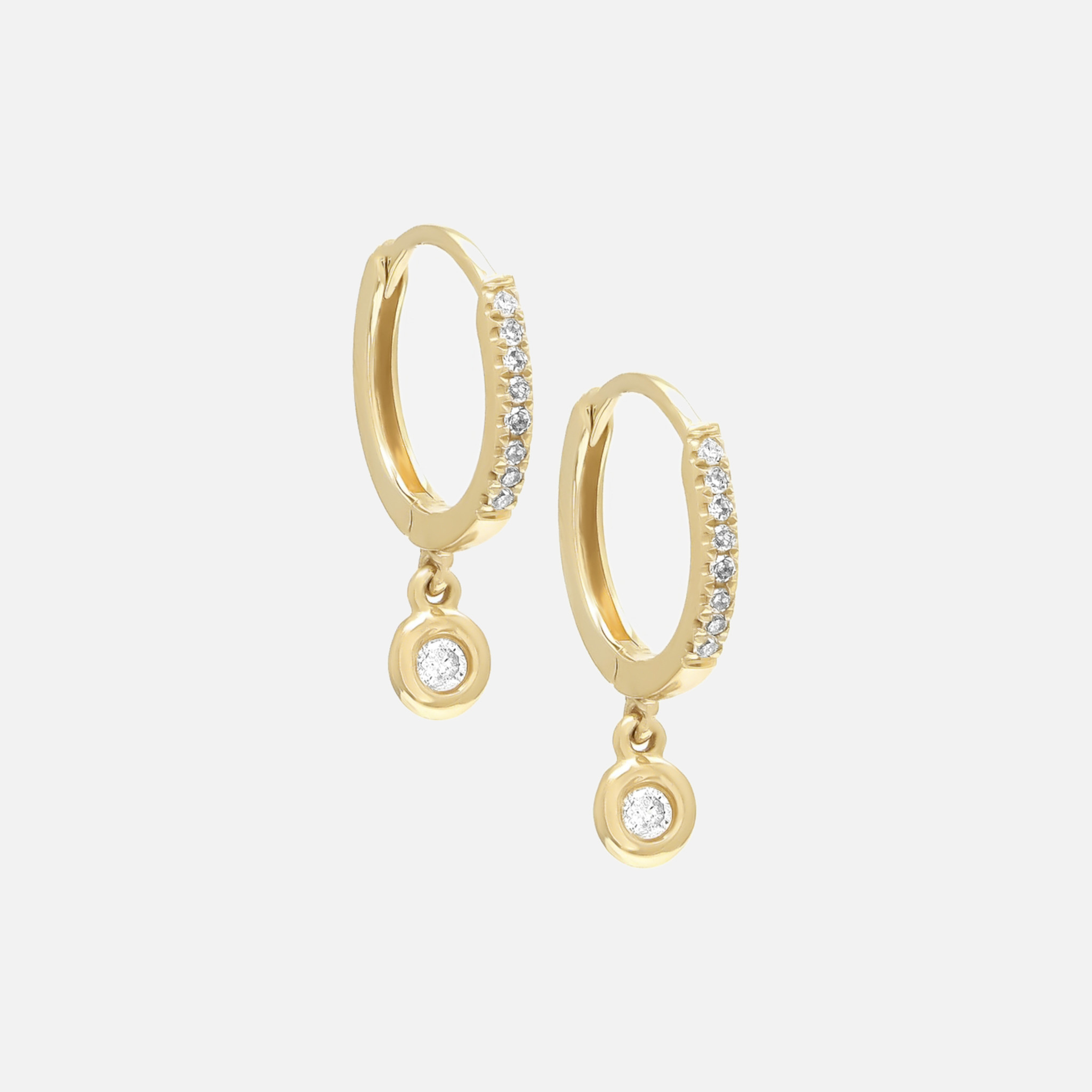 These bezel diamond huggies. Handcrafted in 14k gold and designed with a lobe-hugging curved exterior rendered with dainty round cut diamonds.