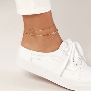 Chic model wearing gold chain necklace around ankle, styled with white shoes.
