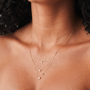 Elegante collar escalonado de oro de 14k con tres diamantes engastados en bisel sobre delicadas cadenas, diseñado para adornar su cuello con belleza, como se ve en una modelo puertorriqueña.