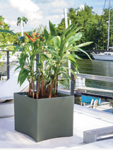 Paso Robles Planter, modern square outdoor plant pot with lush green plants, waterfront marina setting with boats and trees in background.
