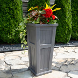 Graphite Gray  Promenade Tall Patio Planter with tropical flowers and evergreen bushes in background