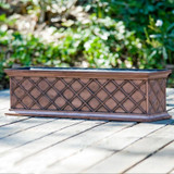 Copper ArmoreCoat La Fleur Railing Planter, a rectangular decorative copper planter with a diamond lattice pattern, placed outdoors on a wooden surface with greenery in the background.