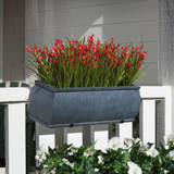 Barrel Fiberstone Railing Planter, a rectangular outdoor planter with a textured gray fiberstone finish, filled with vibrant red flowers, positioned on a white porch railing.