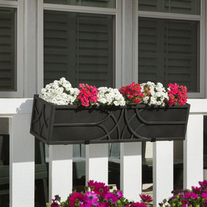Falling Water Railing Planter, black decorative rectangular flower box with pink and white blooming flowers, mounted on a white balcony railing in front of a house with windows and shutters.
