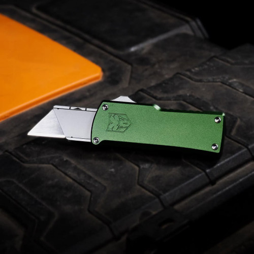 CobraTec green dual-action OTF utility knife on textured black surface with orange accent, 6061-T6 aluminum construction, lightweight 3.2oz EDC design