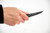 (Forward Grip Close-Up) Hand gripping TOPS El Pionero in forward position | "MADE IN USA BLACKOUT EDITION" blade markings visible | Tactical fixed blade knife with black handle scales