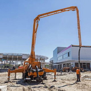 A construction site with an orange concrete pump, a person holding the boom line in position