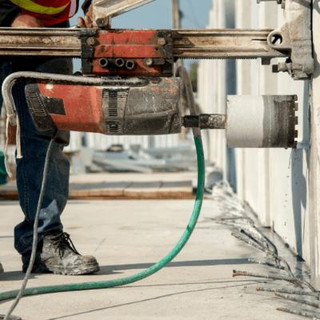 A person using a saw/core drilling machine up against a concrete wall.