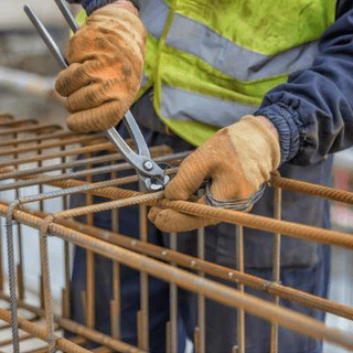 Man wearing PPE securing steel bars together with construction wire.