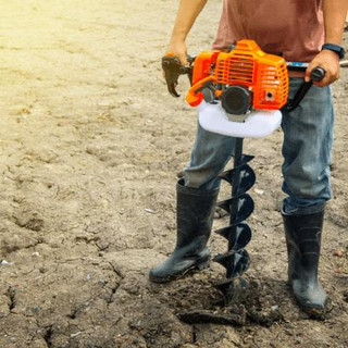 Man wearing jeans and long black gum boots operating a handheld Auger machine.