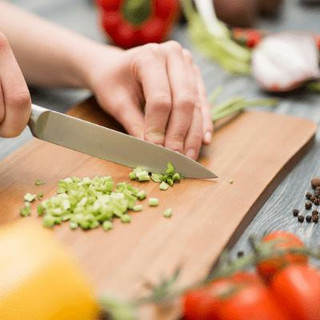 Person cutting vegetables with a kitchen knife on a chopping board.