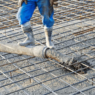 Man standing on a concreting pipe that is releasing concrete into a set area.