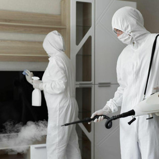 Two workers in head to toe white suits, one using a pressure cleaner, the other spray and wiping a surface