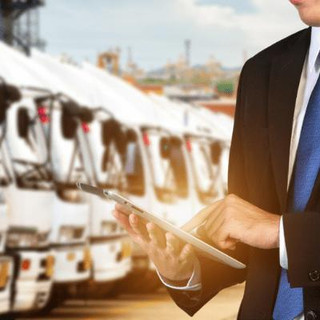 Man wearing a suit checking an ipad with company vehicles lined up in the background.