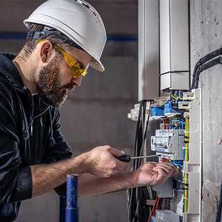 A male electrician works in a switchboard with an electrical connecting cable.