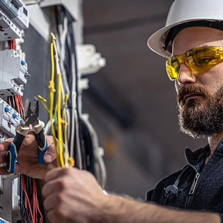 Male electrician works in a switchboard with an electrical connecting cable.