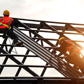 Construction engineer wear safety uniform using an electric drill and screw tools to fasten down metal roofing work.