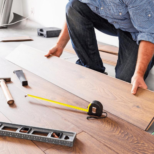 Man installing wooden flooring, using multiple different tools.