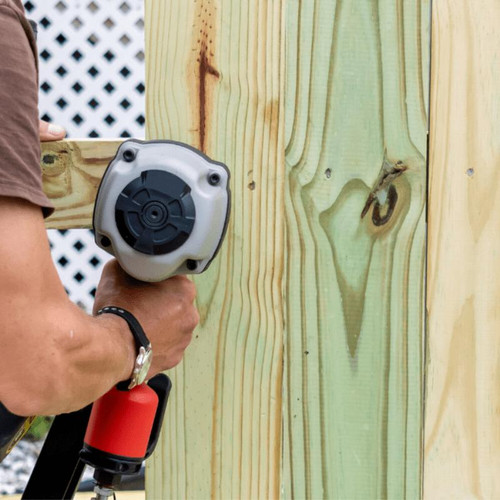 Man working on a fence using a drill.