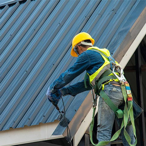 Construction worker wearing safety harness belt during working on roof structure of building on construction site