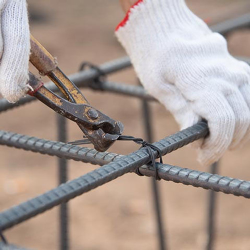 Workers using steel wire and pincers to secure steel rebar reinforcement for concrete at construction site.