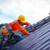 Roofer worker in protective uniform wear and gloves, using air or pneumatic nail gun and installing asphalt shingle on top of the new roof