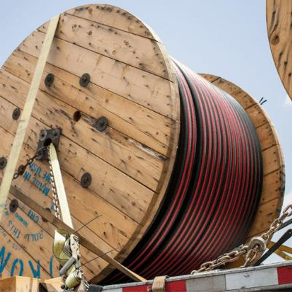 A large roll of cable tied down, being hauled on the back of a truck.