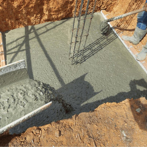 Man working in concrete foundations being poured into excavation.