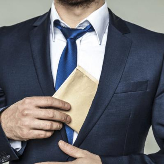 Man in a suit and tie, grabbing a folded up document out of his jacket pocket.