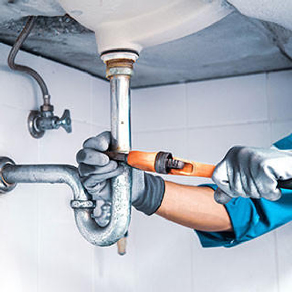 Plumber using a wrench to repair a water pipe under the sink