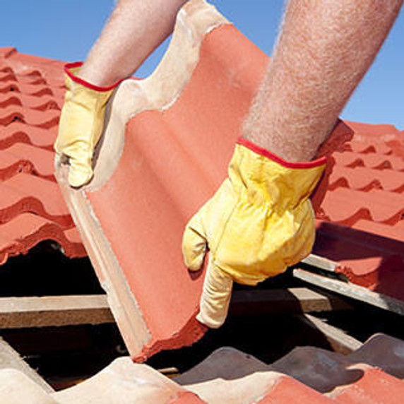 Worker with yellow gloves replacing red tiles or shingles on house
