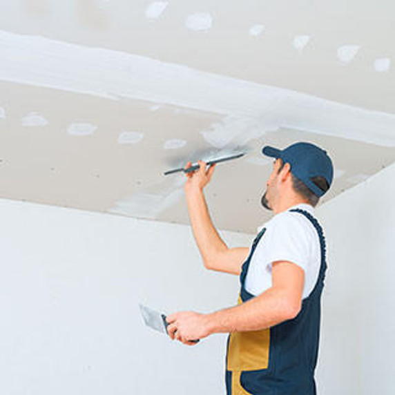 A uniformed worker applies putty to the drywall ceiling