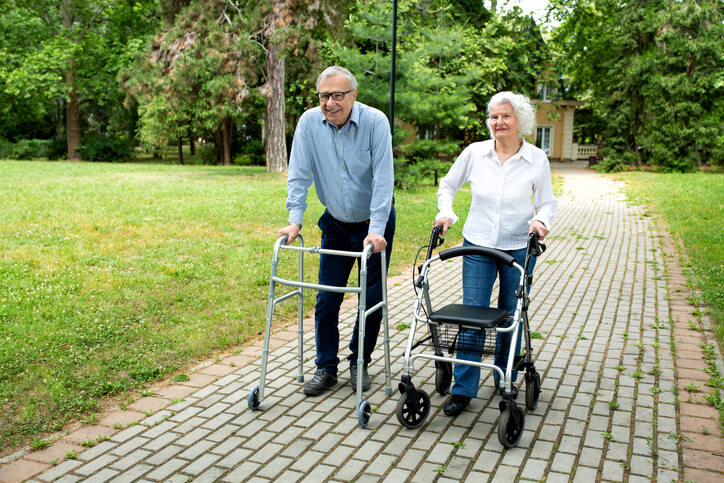 Senior citizens walking through the park one with a walker, one with a rollator.