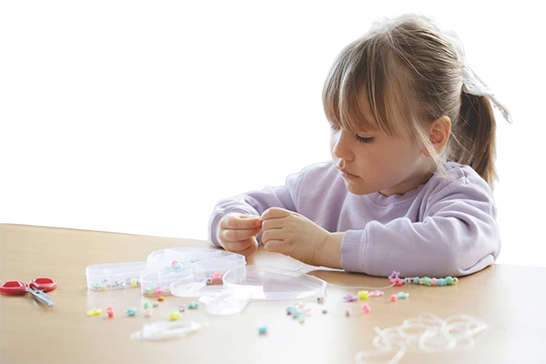 Young girl threading colourful beads onto string at a classroom table