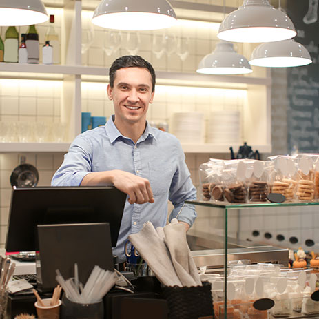 Cafe owner standing at a cash register with flood lighting fixtures overhead