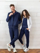 Man and woman medical workers standing in front of a white brick wall wearing navy blue Spirit Scrubs.