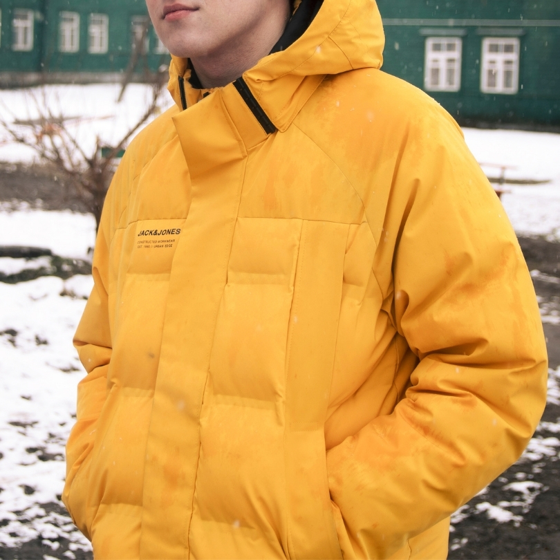 A young man on a snow, wintery walk, wearing a bright yellow winter jacket.