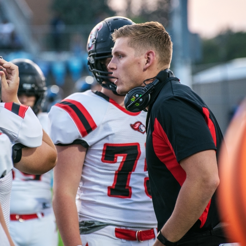 A conversation between a football coach and his team on the sidelines during a NCAA football game