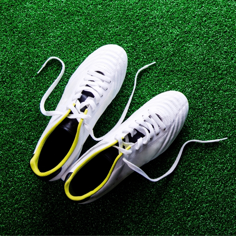 A pair of white and yellow Nike cleats on a football practice field.