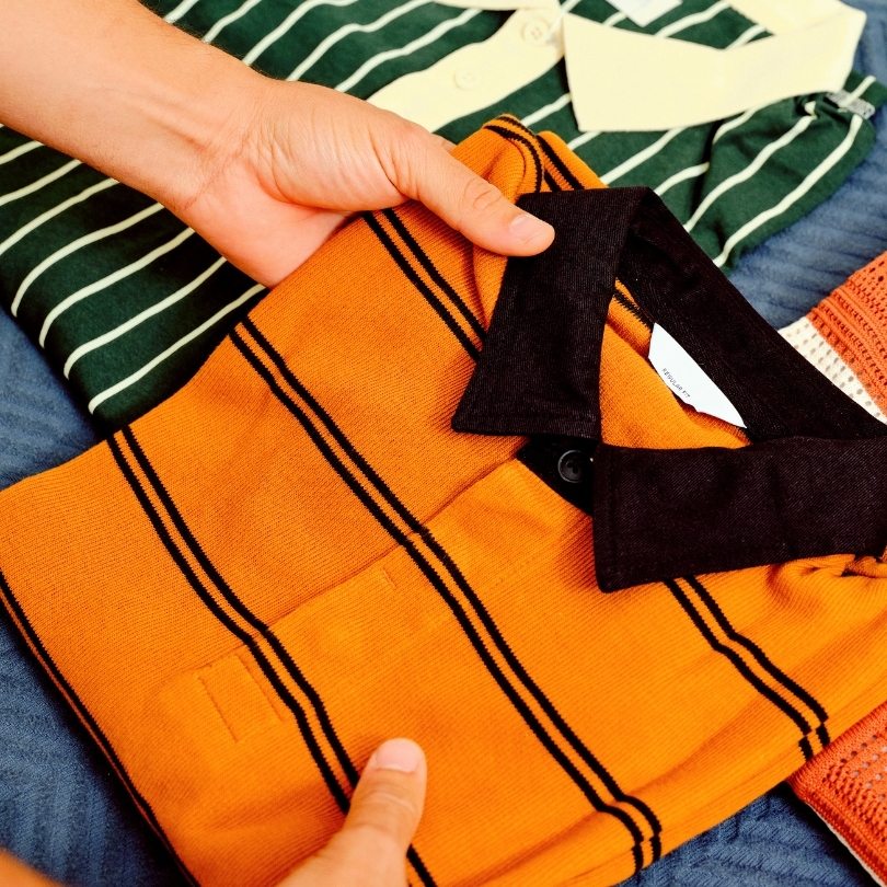 A stack of three polos, with a pair of hands arranging them for review.