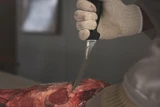 6" curved boning knife cutting through beef held upright