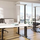 ofinto Stehlampe Lumino Schwarz im modernen Büro - LED-Bürolampe mit grossem Leuchtpanel über höhenverstellbarem Schreibtisch Elevate, ergonomische Arbeitsplatzbeleuchtung in hellem Office mit Parkettboden und Panoramafenster