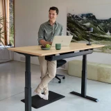 ofinto Ergonomische Stehmatte Schwarz am schwarzen Stehschreibtisch Elevate - Mann in grünem Hemd arbeitet entspannt stehend am Laptop auf schwarzer Anti-Ermüdungsmatte in modernem Home Office mit Bergbild