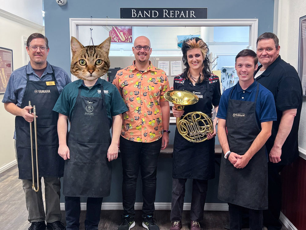 Band repair technicians Maxwell Wasson, James Bauer, Dan Hansen, and Tyler Olsen standing in front of the Murray band repair window wearing Covid masks.