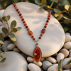 Carnelian Radiance handcrafted gemstone necklace displayed on smooth natural stones with eucalyptus accents, featuring genuine carnelian gemstones and a wire-wrapped pendant by Stone & Story.