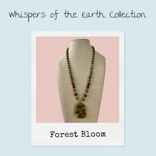 Forest Bloom Necklace from the Whispers of the Earth Collection — a handcrafted gemstone necklace featuring a wire-wrapped Unakite pendant with green Kambaba Jasper and deep red Malaysian Jade beads, accented with golden details and a floral clasp on a neutral display bust