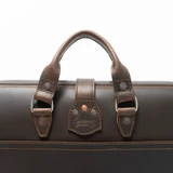 High quality side view of the flight bag leather briefcase in dark brown showing the shoulder strap and two handles for easy carry. Made by Saddleback